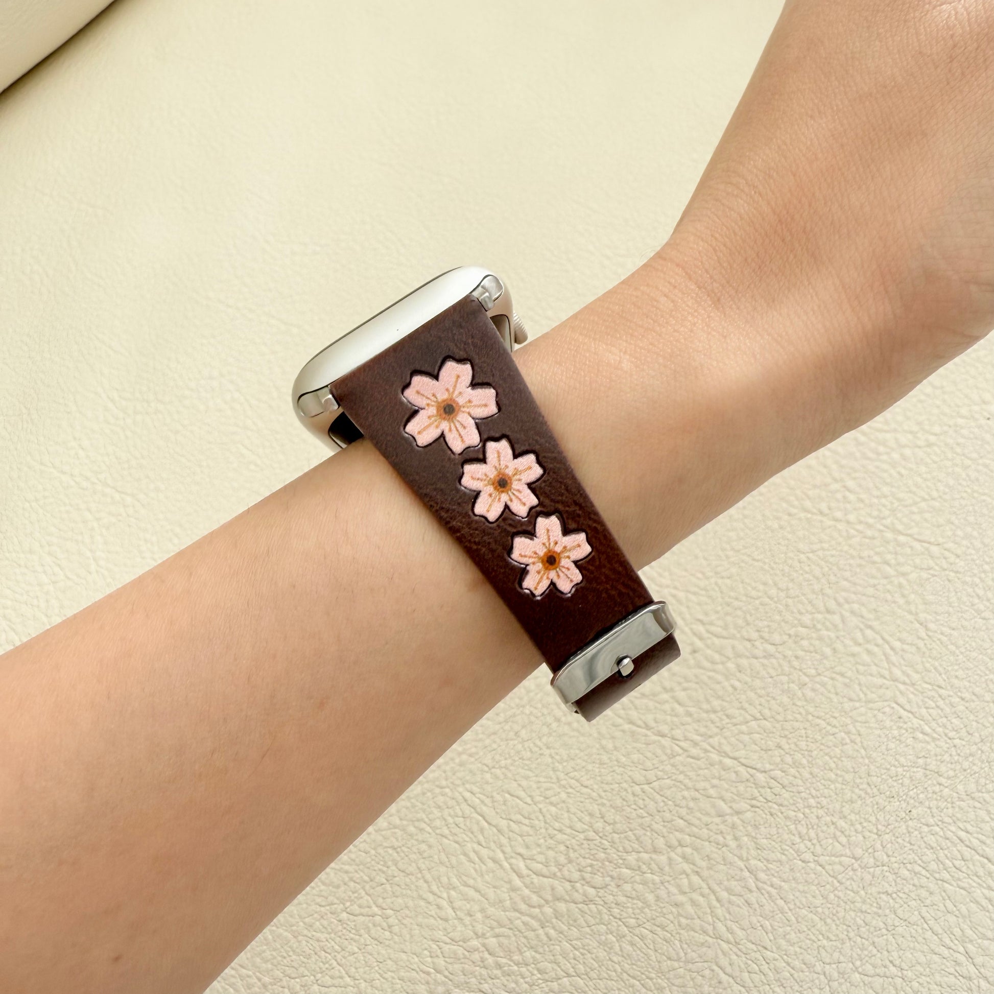 Wrist wearing a brown leather watch strap with pink floral designs