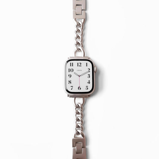 A STARLIGHT-colored metal band Apple Watch bracelet with a starlight finish, displayed alongside a watch face showing time markings.