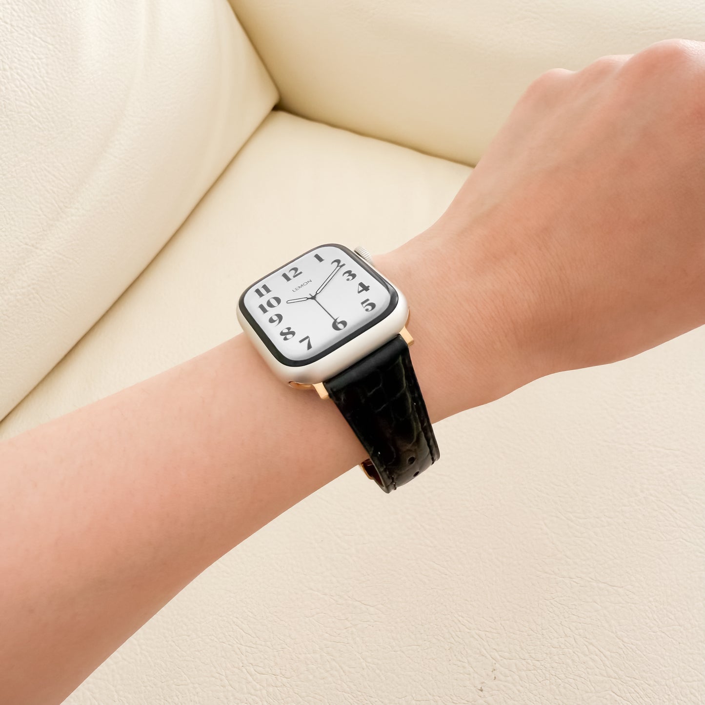 Person wearing a black LEATHER APPLE WATCH wristwatch with a white face on a beige background