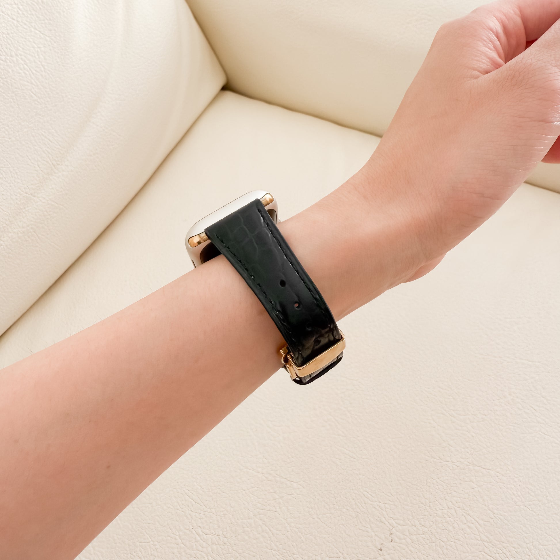 Black watch strap with gold accents on a wrist against a beige background