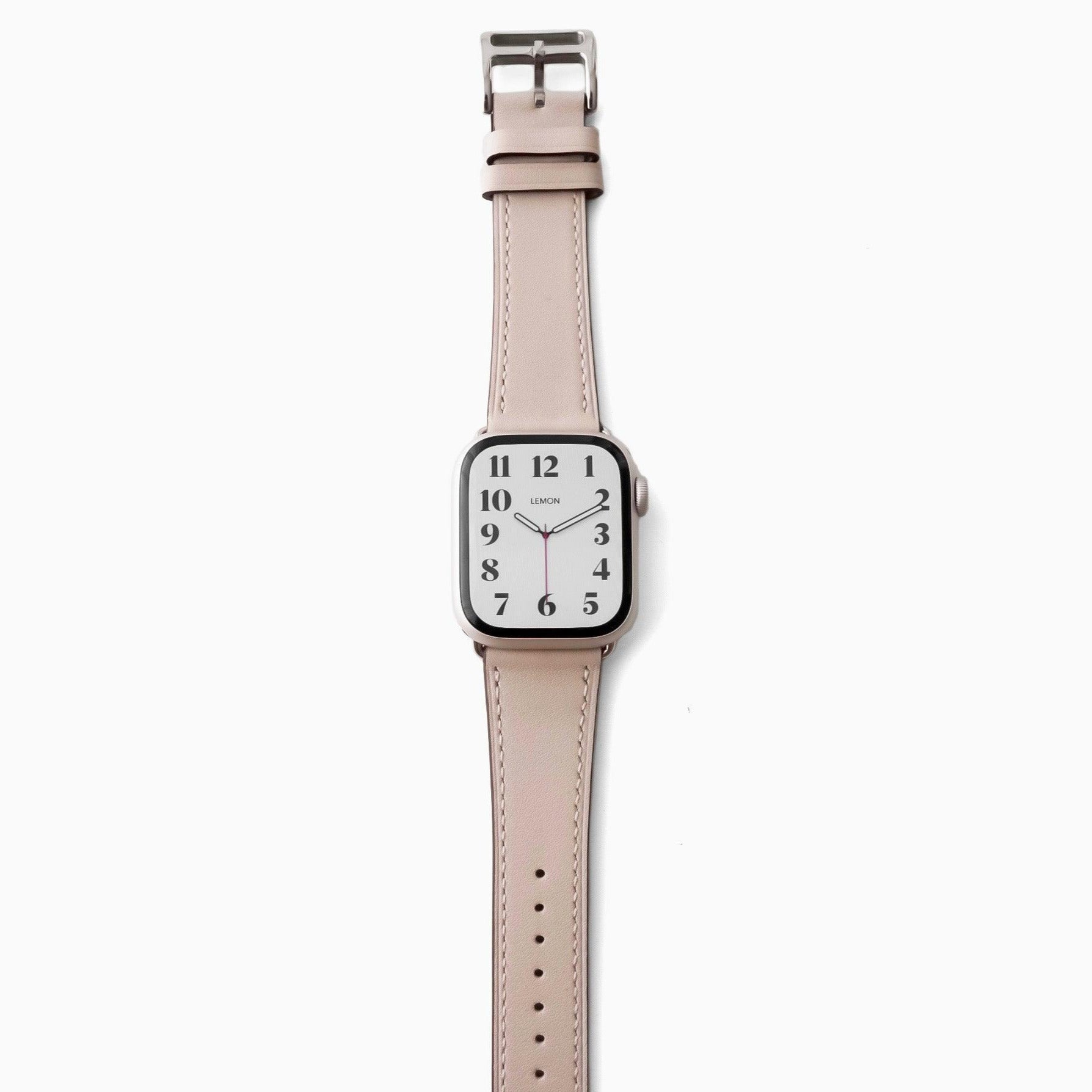 A STARLIGHT BEIGE leather Apple Watch band with a silver buckle and a watch face displaying time and date.