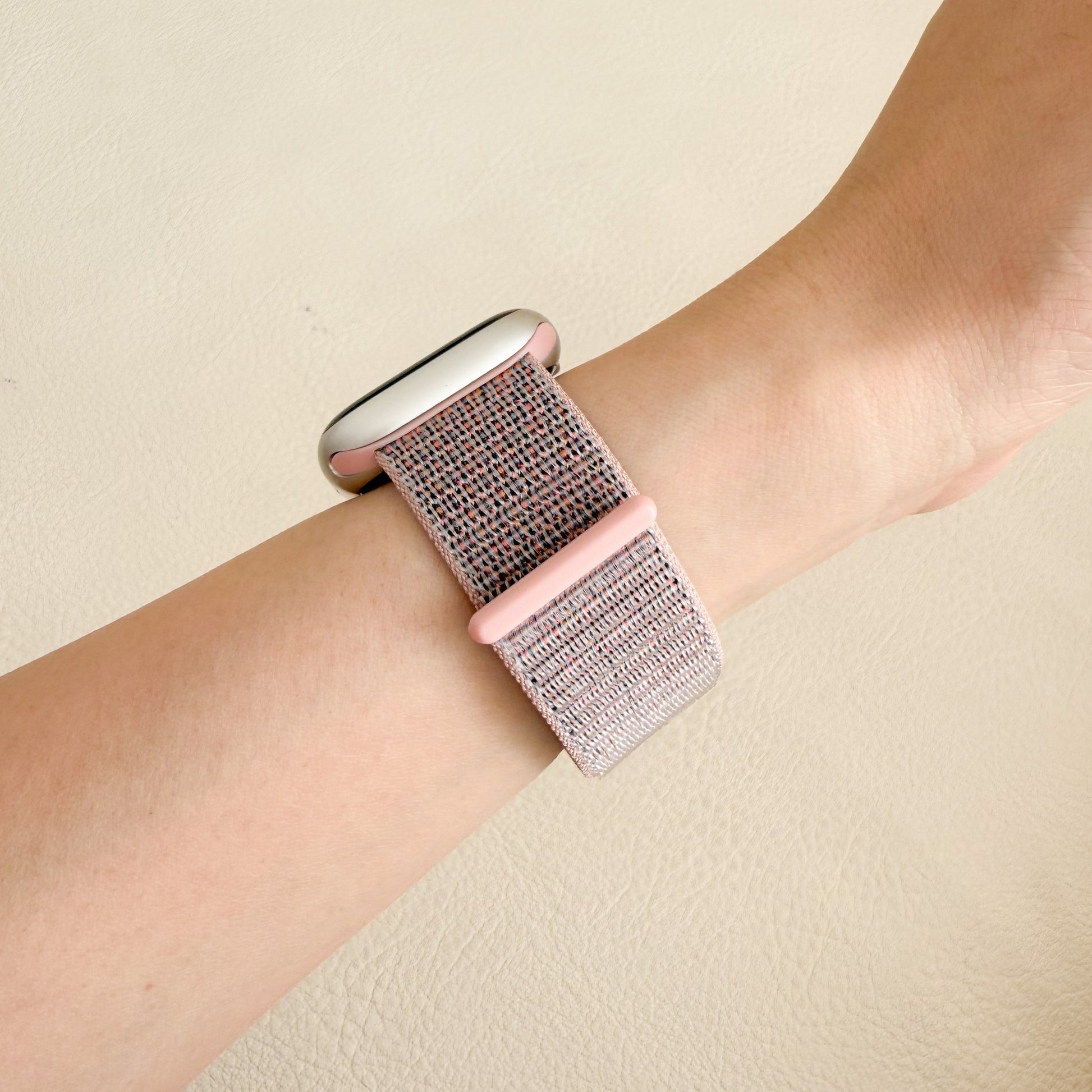 Wrist wearing a pink woven APPLE watch band on a beige background