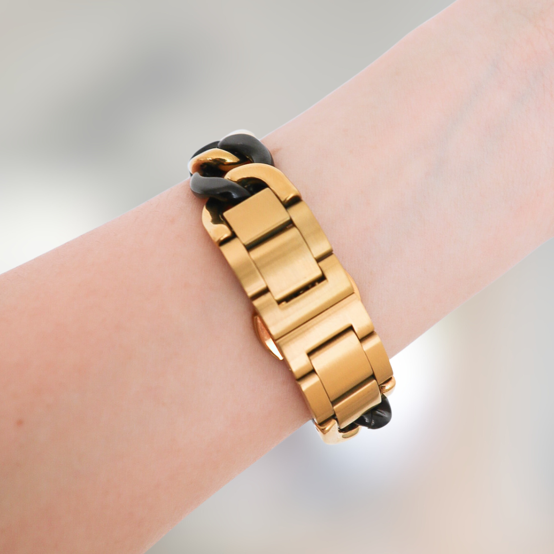 Gold and black bracelet on a wrist against a neutral background
